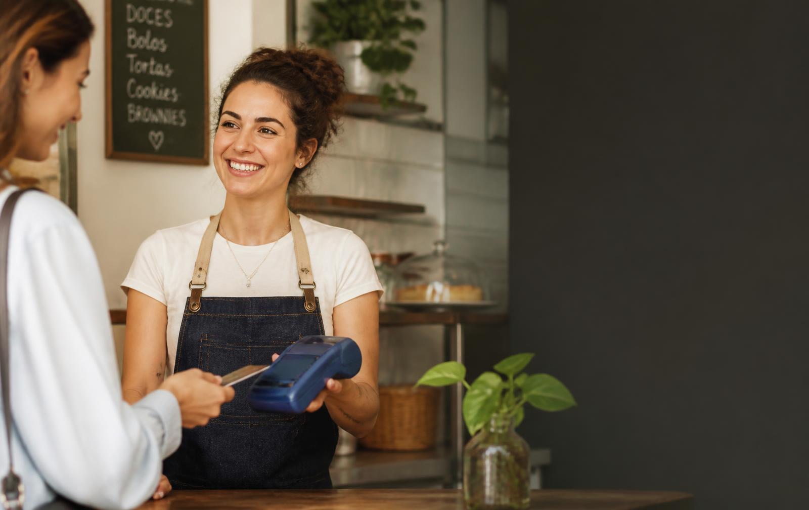Lojista de cafeteria atendendo cliente com máquina de pagamento NILI